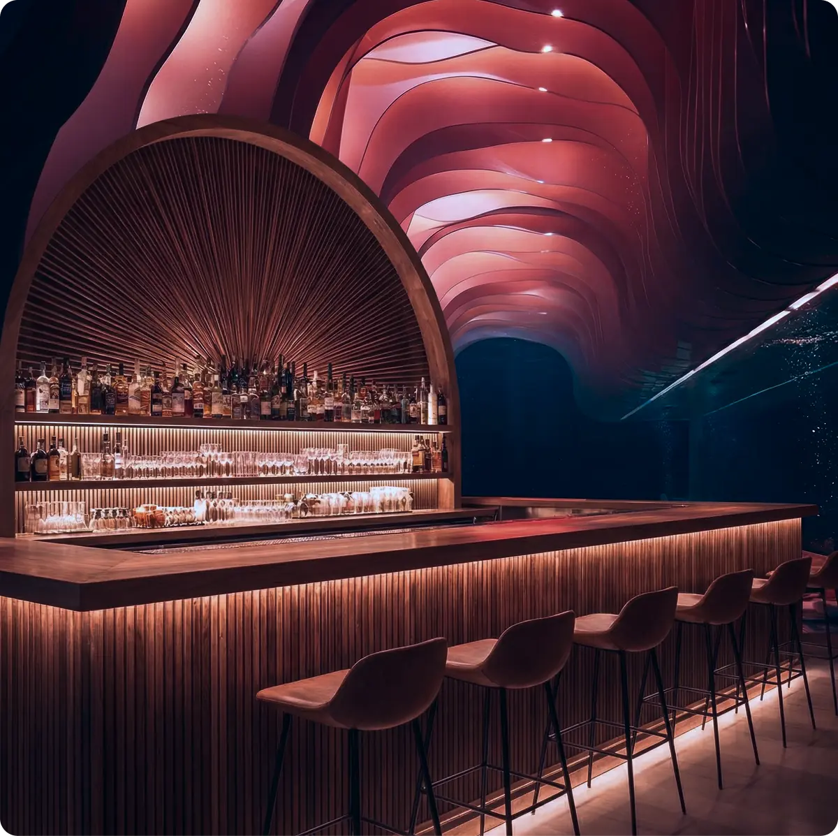 Area bar del ristorante Riff: elegante bancone con espositore ad arco, luci d'atmosfera e il caratteristico soffitto ondulato rosa.